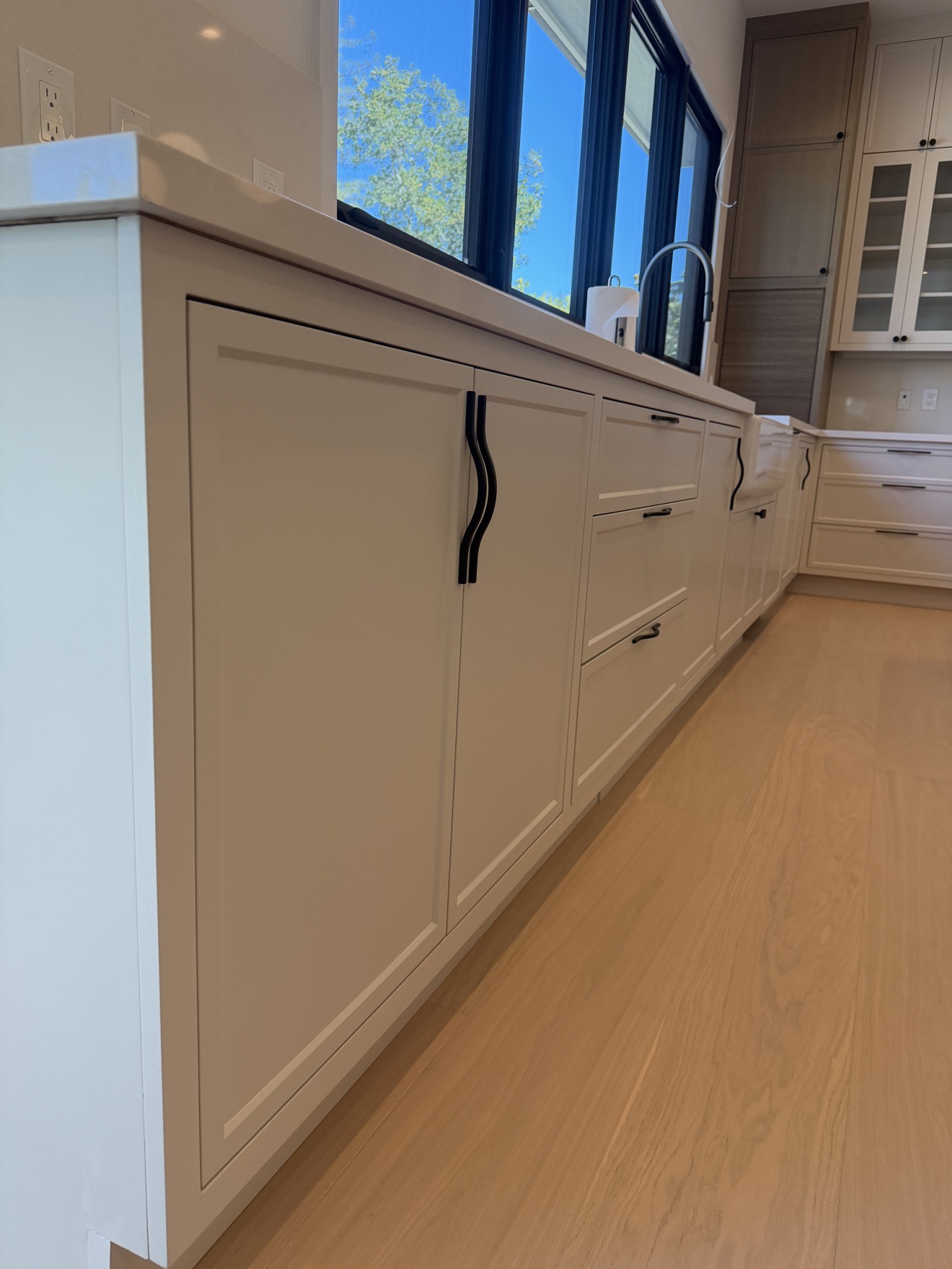 Hillsborough sink base cabinets in painted frameless fronts with sculptural black pulls beneath a run of windows