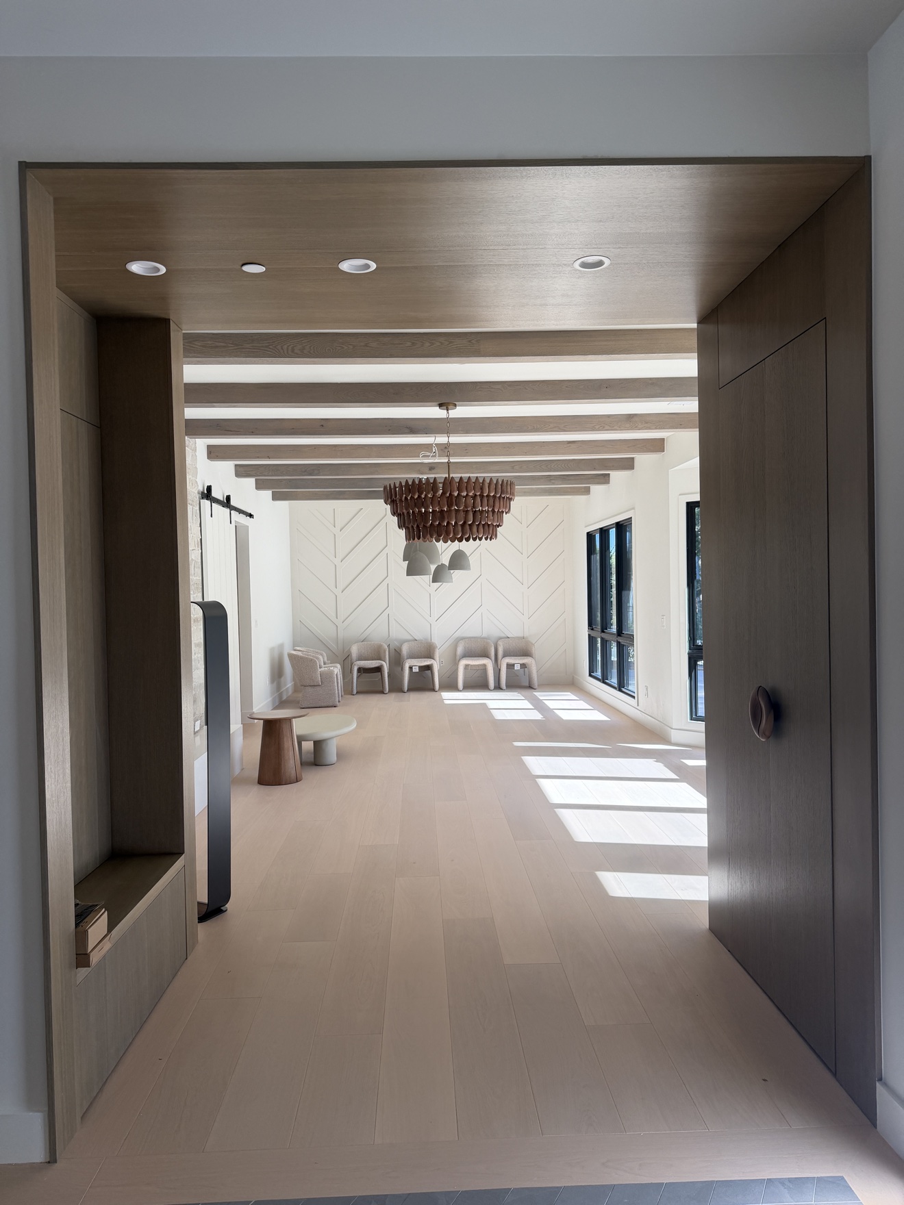 Hillsborough living room viewed through the white oak entry frame, with stained ceiling beams and a chevron accent wall