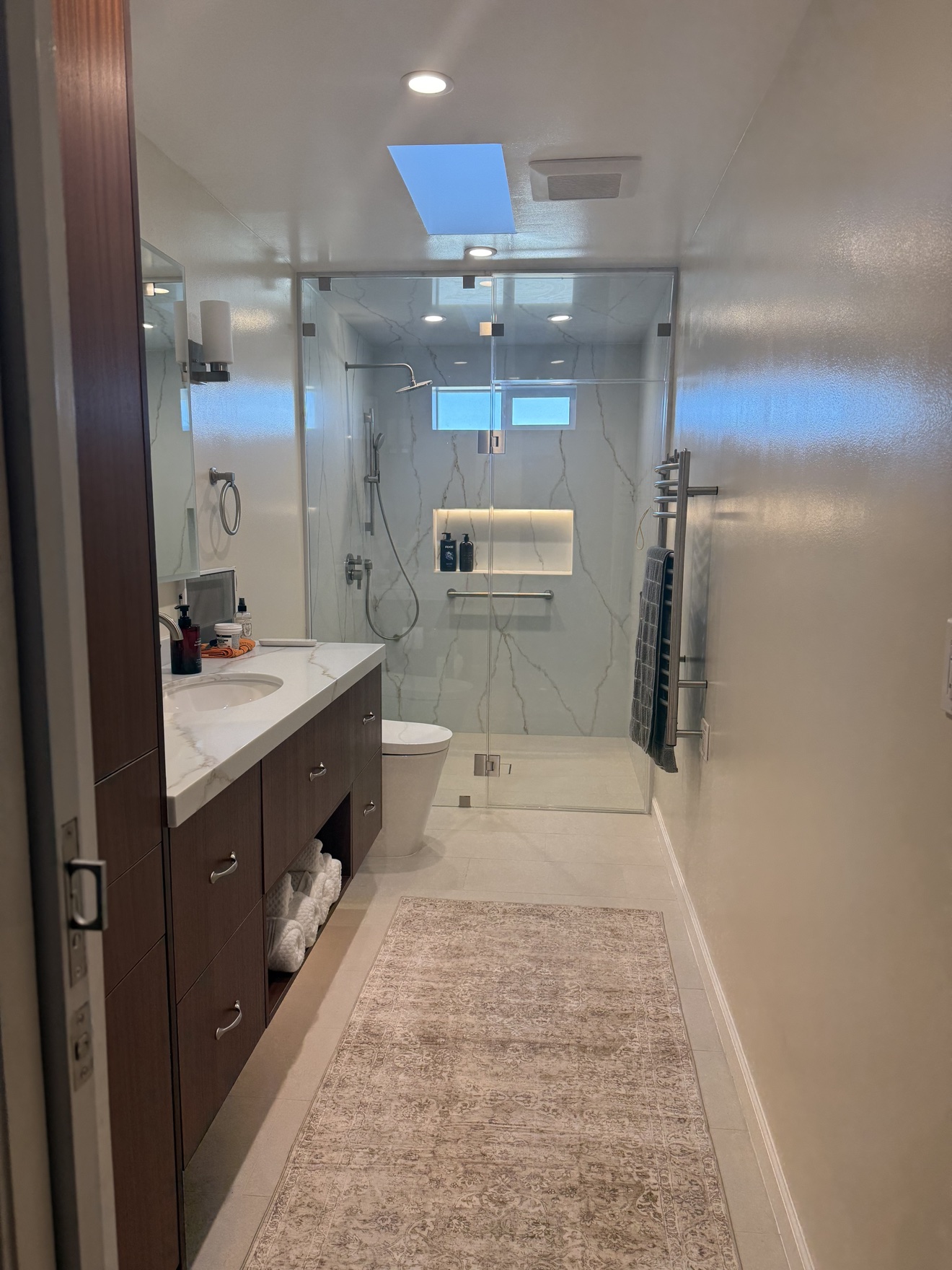 SSF bathroom overview with the walnut vanity, glass-enclosed marble-look shower, and a skylight
