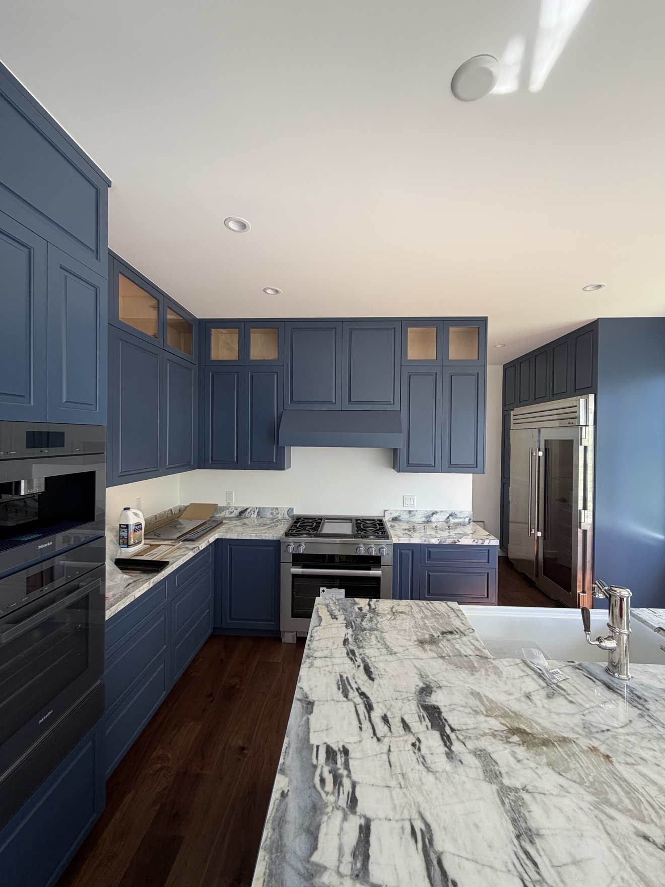 Lombard St blue Shaker kitchen with a veined marble island, glass-front display uppers, and built-in Miele ovens